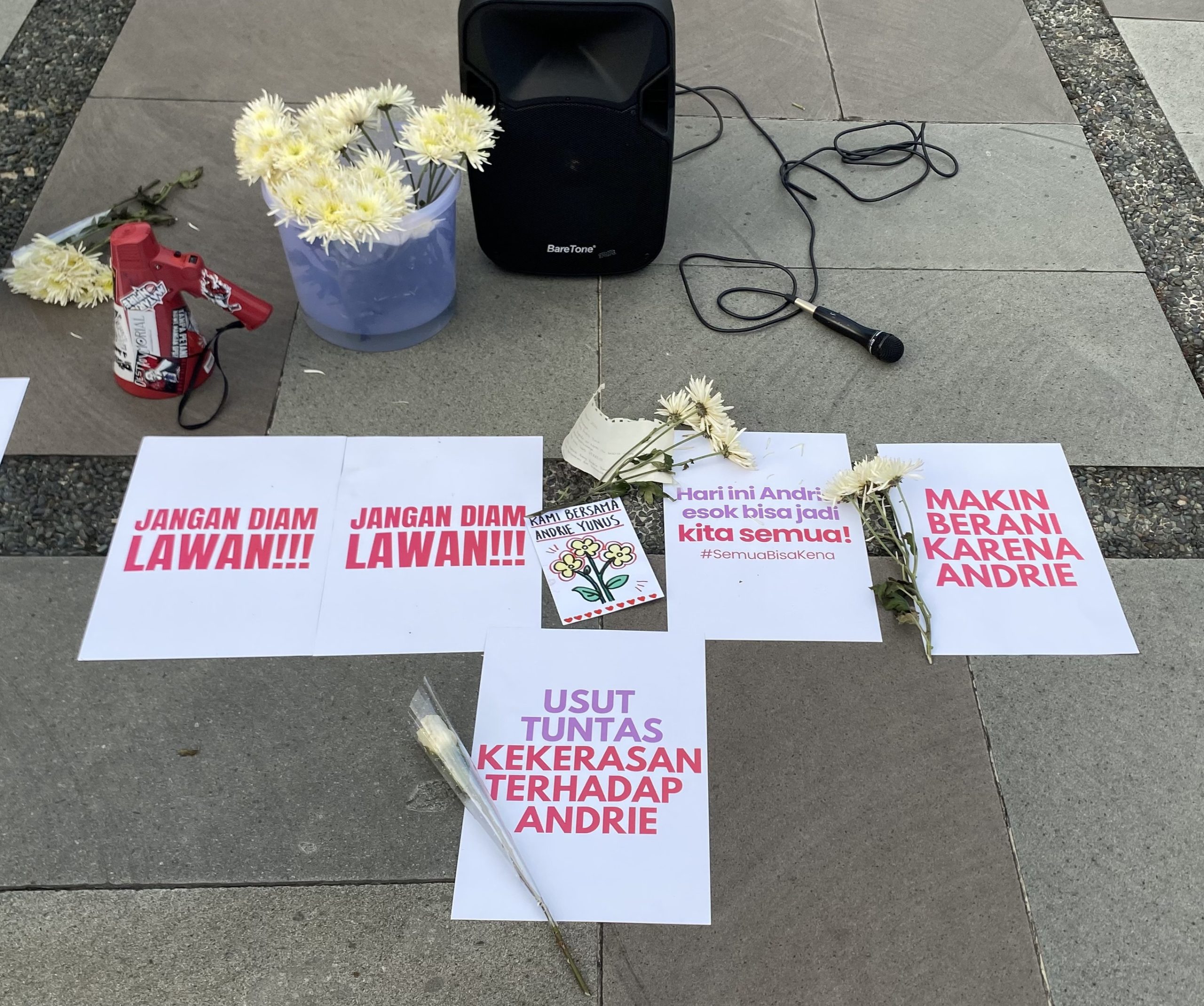 Poster tuntutan serta bunga yang dibagikan peserta aksi.